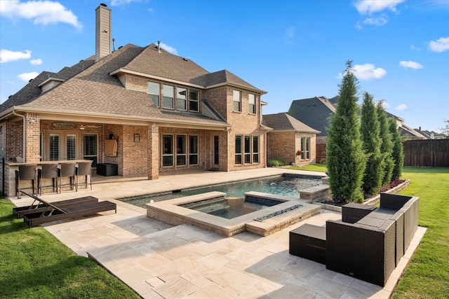1741 Mountain Creek Ln, Prosper, TX 75078 - rear view of house with a patio area, roof with shingles, brick siding, a chimney, and a pool with connected hot tub