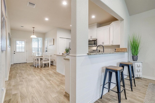 3108 Ridgecrest Dr, Granbury, TX 76048 - kitchen featuring stainless steel microwave, light wood-style floors, white cabinets, a breakfast bar, and recessed lighting