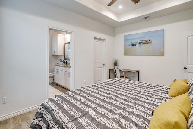 3108 Ridgecrest Dr, Granbury, TX 76048 - bedroom with light wood-style floors, baseboards, connected bathroom, a tray ceiling, and a ceiling fan