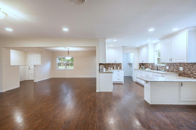 2489 Campus Ct, Abilene, TX 79601 - kitchen with white cabinets, a peninsula, decorative backsplash, dark wood-type flooring, and light stone counters