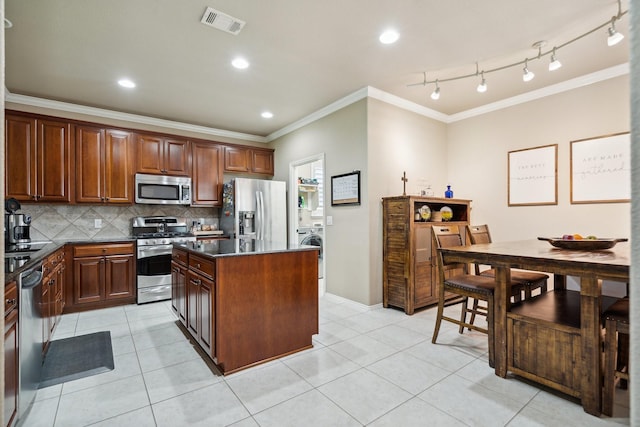 6173 Arcadia Park Ln, Frisco, TX 75036 - kitchen with appliances with stainless steel finishes, crown molding, a kitchen island, dark countertops, and washer / clothes dryer