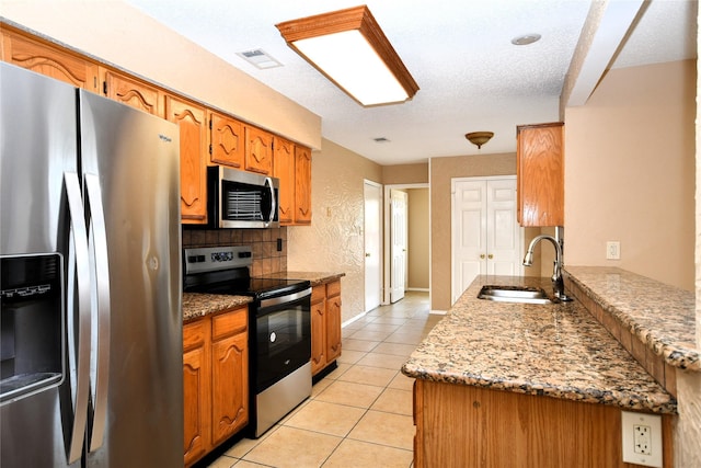 2906 Kingswood Dr, Garland, TX 75040 - kitchen featuring stainless steel appliances, a sink, light tile patterned floors, a peninsula, and brown cabinetry