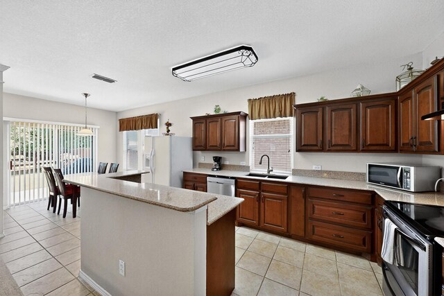 848 Ridge Point Dr, Grand Prairie, TX 75052 - kitchen with appliances with stainless steel finishes, light tile patterned floors, a kitchen island, decorative light fixtures, and a textured ceiling