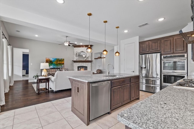 350 Lake Trail Ln, Prosper, TX 75078 - kitchen featuring stainless steel appliances, a sink, a ceiling fan, a glass covered fireplace, and light tile patterned floors