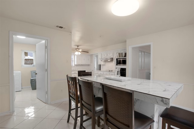 9718 Burney Dr, Dallas, TX 75243 - kitchen with white cabinets, stainless steel microwave, a breakfast bar, and under cabinet range hood