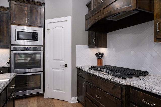 2113 Twin Creeks Cir, Pilot Point, TX 76258 - kitchen with stainless steel appliances, dark brown cabinets, exhaust hood, and light stone counters