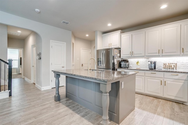 240 Gill Point Ln, Aledo, TX 76008 - kitchen with stainless steel fridge with ice dispenser, a sink, light wood finished floors, arched walkways, and white cabinets