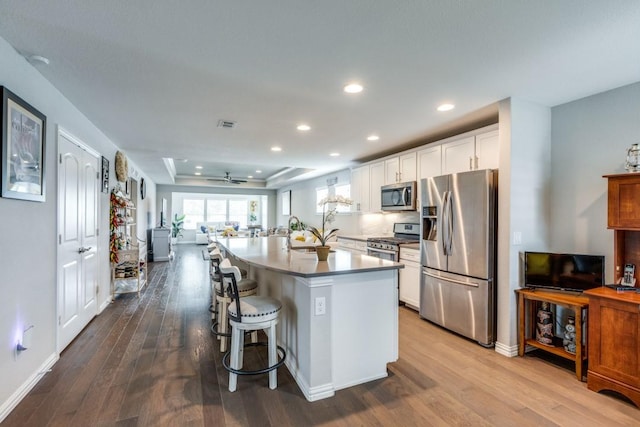7812 Gulf Breeze Ln, Frisco, TX 75036 - kitchen featuring appliances with stainless steel finishes, white cabinetry, wood finished floors, a tray ceiling, and a breakfast bar