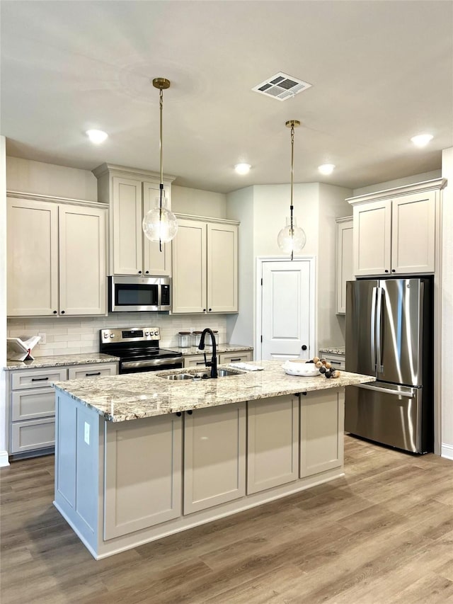 358 Frederick Dr, Robinson, TX 76706 - kitchen with appliances with stainless steel finishes, a sink, light wood-type flooring, a center island with sink, and decorative light fixtures