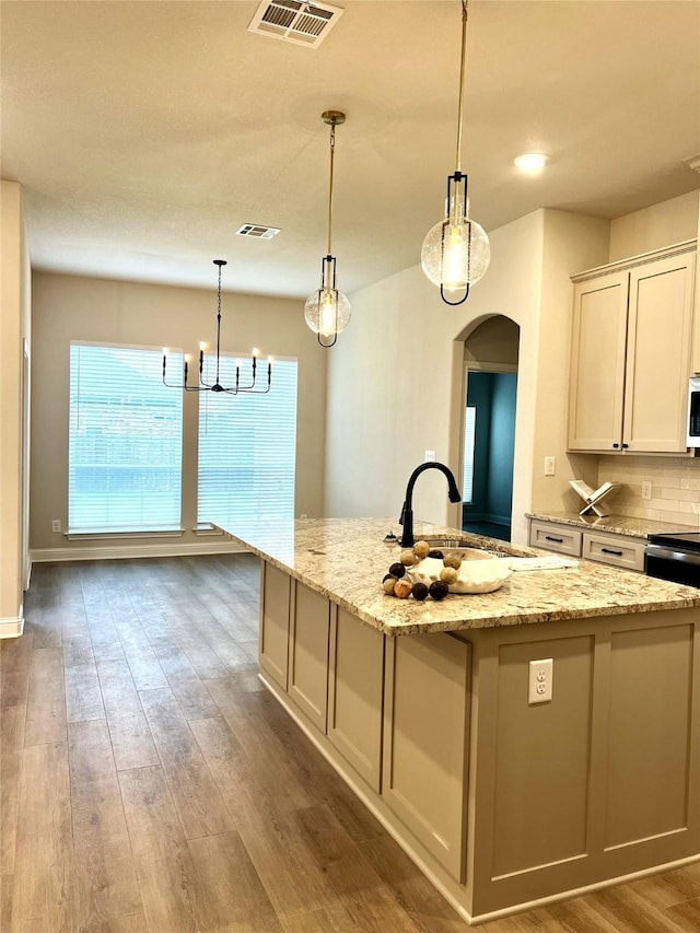 358 Frederick Dr, Robinson, TX 76706 - kitchen featuring a sink, arched walkways, wood finished floors, a kitchen island with sink, and light stone countertops