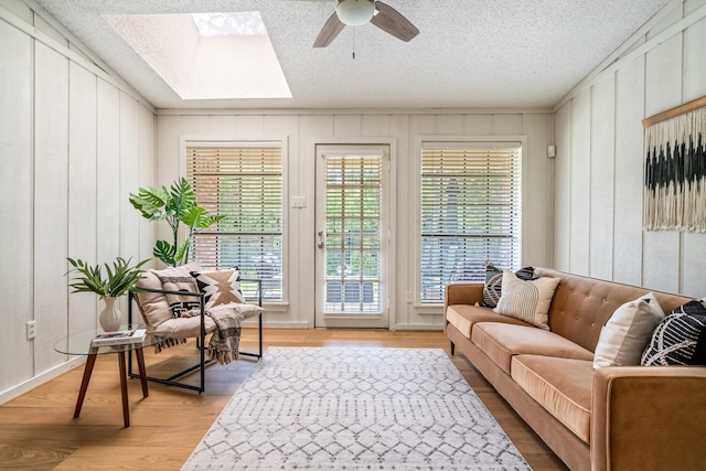 6737 Lake Shore Dr, Garland, TX 75044 - living area featuring a skylight, light wood finished floors, a ceiling fan, a decorative wall, and a textured ceiling