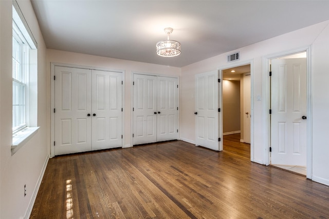 3635 Merrell Rd, Dallas, TX 75229 - unfurnished bedroom with multiple closets, baseboards, wood finished floors, and a chandelier