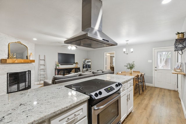 559 Bell Dr, Allen, TX 75002 - kitchen with stainless steel range with electric stovetop, island exhaust hood, white cabinetry, light stone counters, and a fireplace