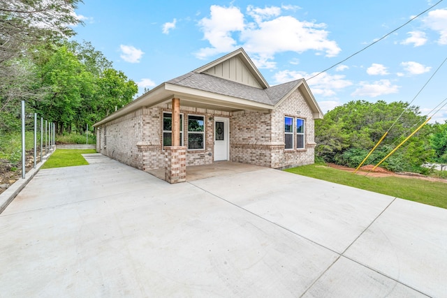 915 Comanche Cove Dr, Granbury, TX 76048 - view of front facade with board and batten siding, brick siding, a front lawn, a patio area, and a shingled roof
