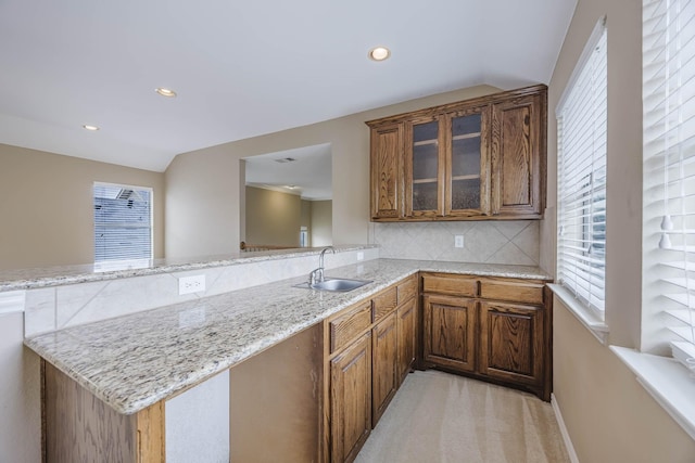 7605 Chief Spotted Tail Dr, Mckinney, TX 75070 - kitchen featuring a sink, a peninsula, light stone counters, glass insert cabinets, and decorative backsplash