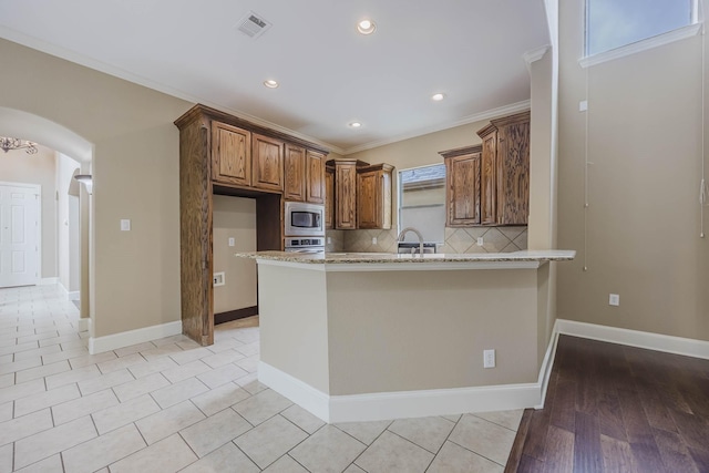 7605 Chief Spotted Tail Dr, Mckinney, TX 75070 - kitchen with appliances with stainless steel finishes, arched walkways, light stone countertops, a peninsula, and tasteful backsplash