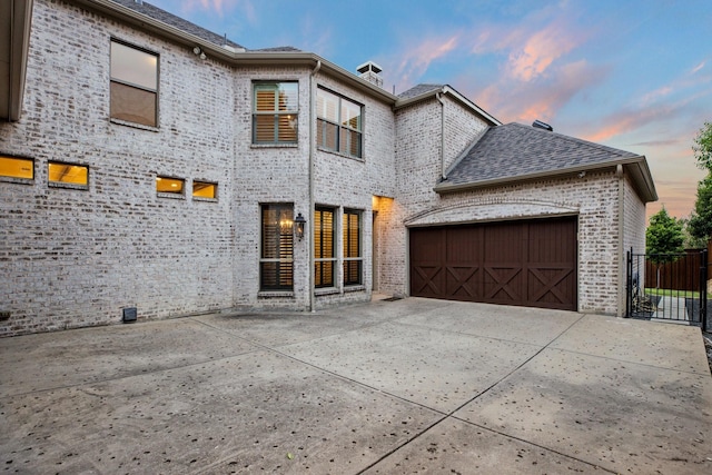 6131 Arboretum Dr, Frisco, TX 75034 - back of house at dusk with brick siding, driveway, an attached garage, and roof with shingles