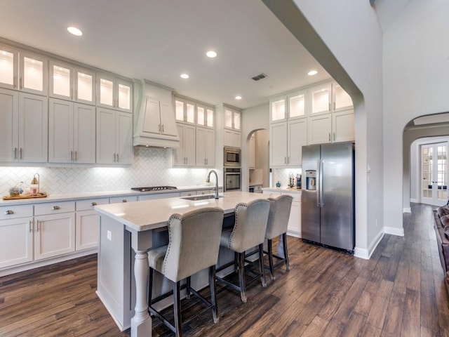 3051 Kennington Dr, Prosper, TX 75078 - kitchen featuring appliances with stainless steel finishes, arched walkways, a sink, premium range hood, and a center island with sink