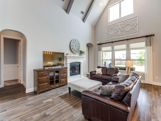 3051 Kennington Dr, Prosper, TX 75078 - living area featuring high vaulted ceiling, arched walkways, wood finished floors, beam ceiling, and a glass covered fireplace