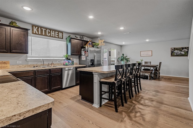 129 Clear Creek Ln, Terrell, TX 75160 - kitchen with stainless steel appliances, a sink, a kitchen bar, dark brown cabinets, and light wood-style floors