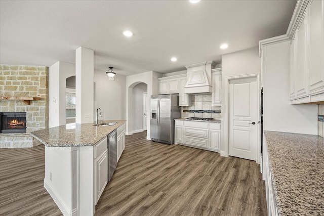 946 Mangrove Dr, Fate, TX 75087 - kitchen featuring stainless steel appliances, custom range hood, arched walkways, a sink, and dark wood-style flooring