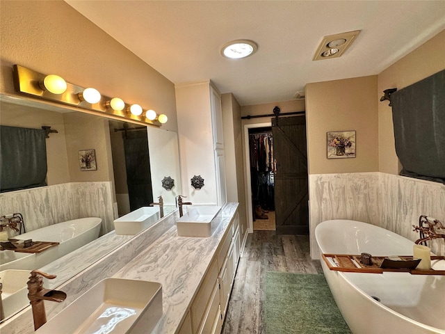 13449 S Hillcreek Rd, Whitehouse, TX 75791 - full bathroom featuring wood finished floors, double vanity, a soaking tub, a walk in closet, and wainscoting