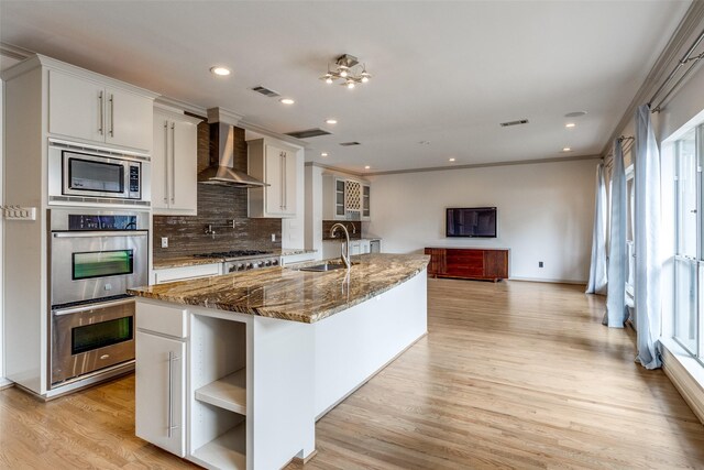 3719 Douglas Ave, Dallas, TX 75219 - kitchen with wall chimney range hood, stainless steel appliances, open shelves, tasteful backsplash, and light wood finished floors