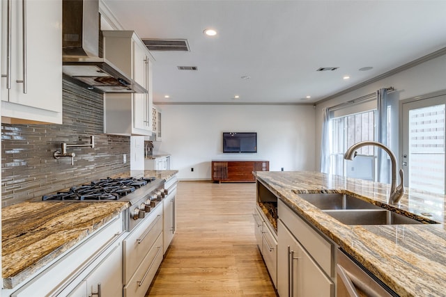3719 Douglas Ave, Dallas, TX 75219 - kitchen with wall chimney range hood, appliances with stainless steel finishes, backsplash, light wood-type flooring, and white cabinets