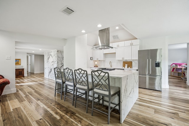 6607 Leameadow Dr, Dallas, TX 75248 - kitchen featuring stainless steel refrigerator with ice dispenser, island exhaust hood, a kitchen bar, white cabinets, and light wood-style floors