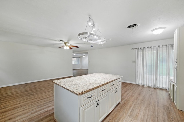 325 Belmont St, Hurst, TX 76053 - kitchen with a ceiling fan, light wood-style floors, a kitchen island, light stone counters, and white cabinetry