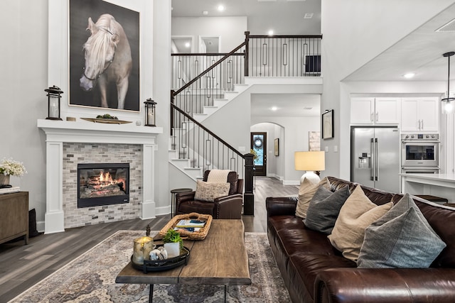 16471 Prairie Oak Rd, Frisco, TX 75033 - living area with dark wood-style floors, stairs, a tiled fireplace, arched walkways, and a towering ceiling