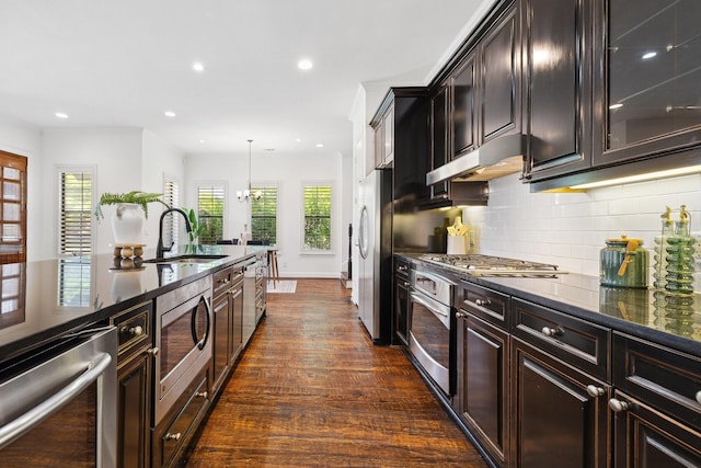 1120 Hemingway Ln, Irving, TX 75063 - kitchen featuring stainless steel appliances, under cabinet range hood, dark wood-style flooring, a sink, and dark stone counters