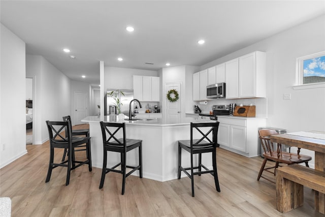 2939 Peony Dr, Sherman, TX 75092 - kitchen with appliances with stainless steel finishes, a kitchen bar, light wood-style floors, white cabinetry, and recessed lighting