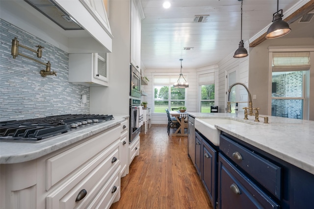 9410 Tay Ln, Justin, TX 76247 - kitchen featuring blue cabinets, stainless steel appliances, wall chimney range hood, wood finished floors, and white cabinetry