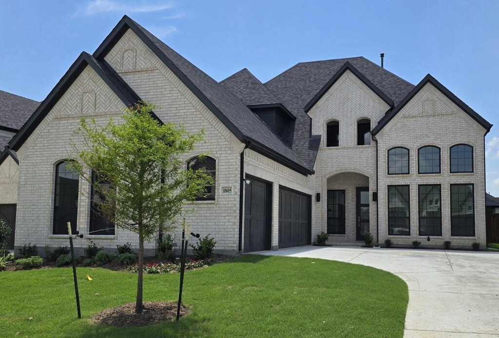 1805 Gem Dr, Rockwall, TX 75087 - french country home with brick siding, driveway, a front yard, an attached garage, and a shingled roof
