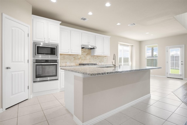4104 Portola Dr, Mckinney, TX 75070 - kitchen featuring appliances with stainless steel finishes, light tile patterned floors, under cabinet range hood, white cabinets, and backsplash
