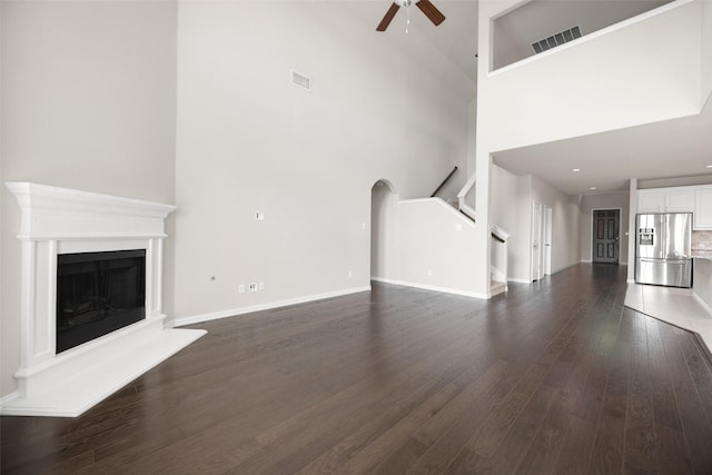 4104 Portola Dr, Mckinney, TX 75070 - unfurnished living room featuring ceiling fan, dark wood-type flooring, a high ceiling, a fireplace with raised hearth, and stairway
