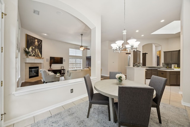 945 Brentwood Dr, Murphy, TX 75094 - dining room featuring a glass covered fireplace, light tile patterned flooring, arched walkways, a ceiling fan, and a chandelier