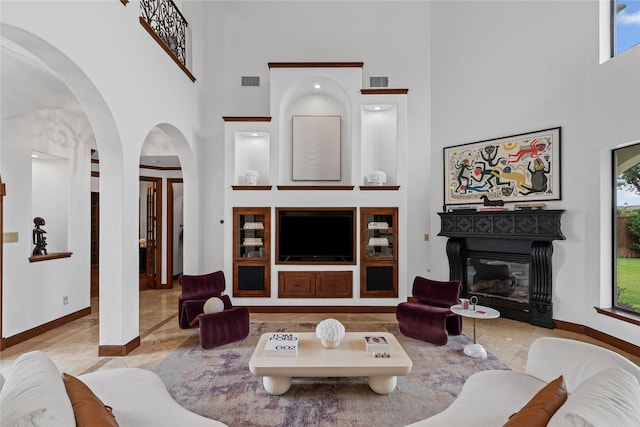 10388 Tobias Ln, Frisco, TX 75033 - living room with a towering ceiling, a glass covered fireplace, baseboards, arched walkways, and tile patterned flooring