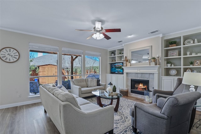 2904 Coventry Ln, Mckinney, TX 75069 - living room featuring a tile fireplace, wood finished floors, ceiling fan, baseboards, and built in shelves