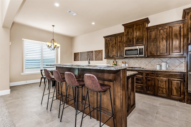 4312 Oxbow Dr, Mckinney, TX 75072 - kitchen featuring stainless steel microwave, a kitchen island, a breakfast bar area, backsplash, and light stone counters