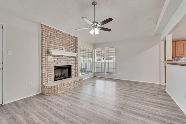 1326 Rosewood Ln, Lancaster, TX 75146 - unfurnished living room with a ceiling fan, light wood-type flooring, a brick fireplace, baseboards, and a textured ceiling