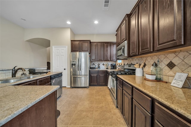 583 Louder Way, Fate, TX 75087 - kitchen with appliances with stainless steel finishes, a sink, dark brown cabinetry, tasteful backsplash, and light stone counters