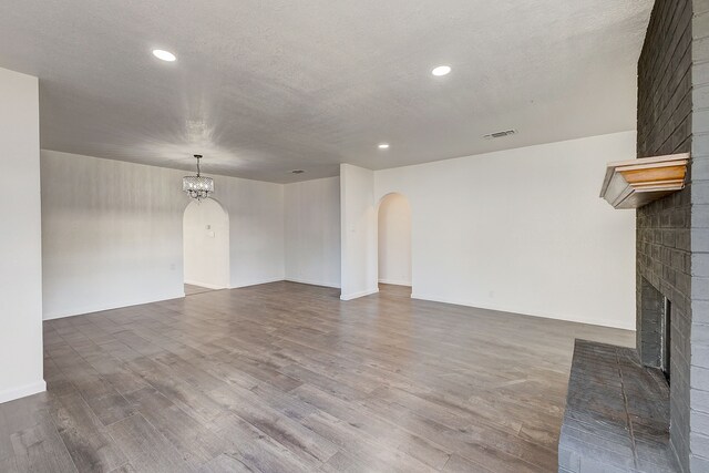 816 Northwood Rd, Fort Worth, TX 76107 - unfurnished living room featuring arched walkways, a brick fireplace, a chandelier, wood finished floors, and a textured ceiling