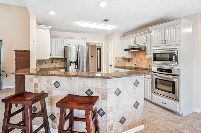 928 Rush Creek Rd, Keller, TX 76248 - kitchen featuring stainless steel appliances, under cabinet range hood, a peninsula, light tile patterned floors, and stone counters