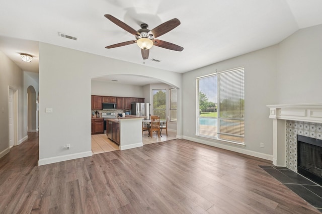 711 Mason Ln, Waxahachie, TX 75167 - unfurnished living room with arched walkways, a fireplace, light wood-style floors, and ceiling fan