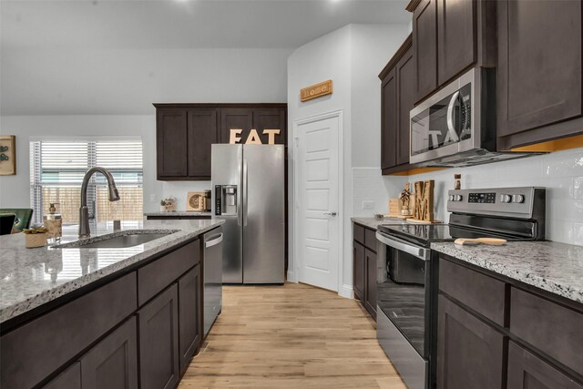 2309 Normandy Ave, Anna, TX 75409 - kitchen featuring stainless steel appliances, a sink, dark brown cabinetry, light wood-type flooring, and light stone countertops
