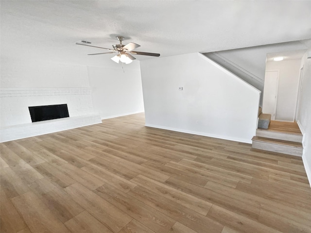 7620 Clover Ln, Watauga, TX 76148 - unfurnished living room with light wood finished floors, ceiling fan, stairway, and a brick fireplace