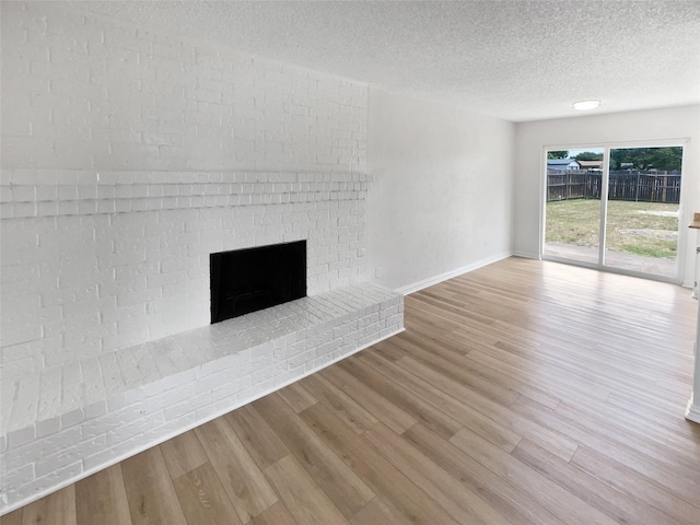 7620 Clover Ln, Watauga, TX 76148 - unfurnished living room featuring wood finished floors, baseboards, a textured ceiling, and a brick fireplace