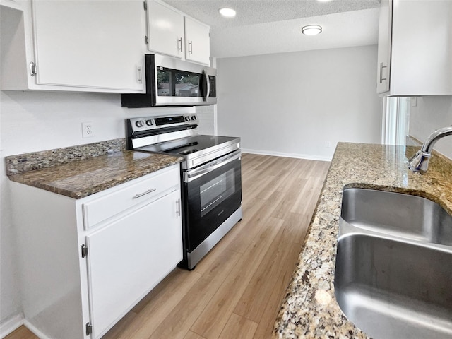 7620 Clover Ln, Watauga, TX 76148 - kitchen featuring appliances with stainless steel finishes, a sink, light wood finished floors, white cabinetry, and dark stone countertops